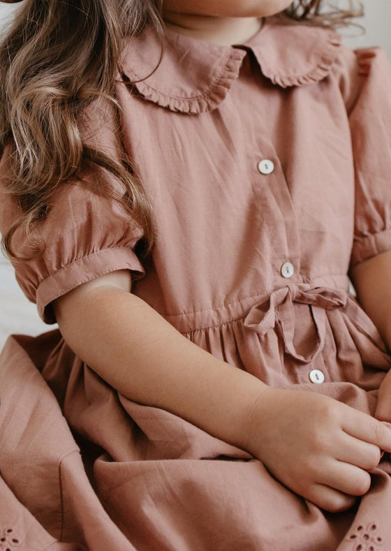 girl wearing a brown dress wth collar and buttons and a tie waist